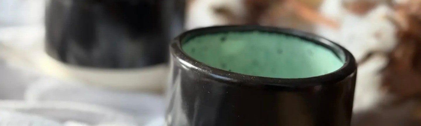 Black and white ceramic cup with legs on a wooden surface, featuring a greenish interior.