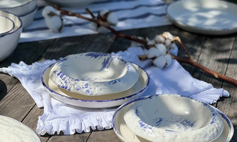 Cream-colored ceramic plates with purple accents on a wooden table decorated with a cotton branch