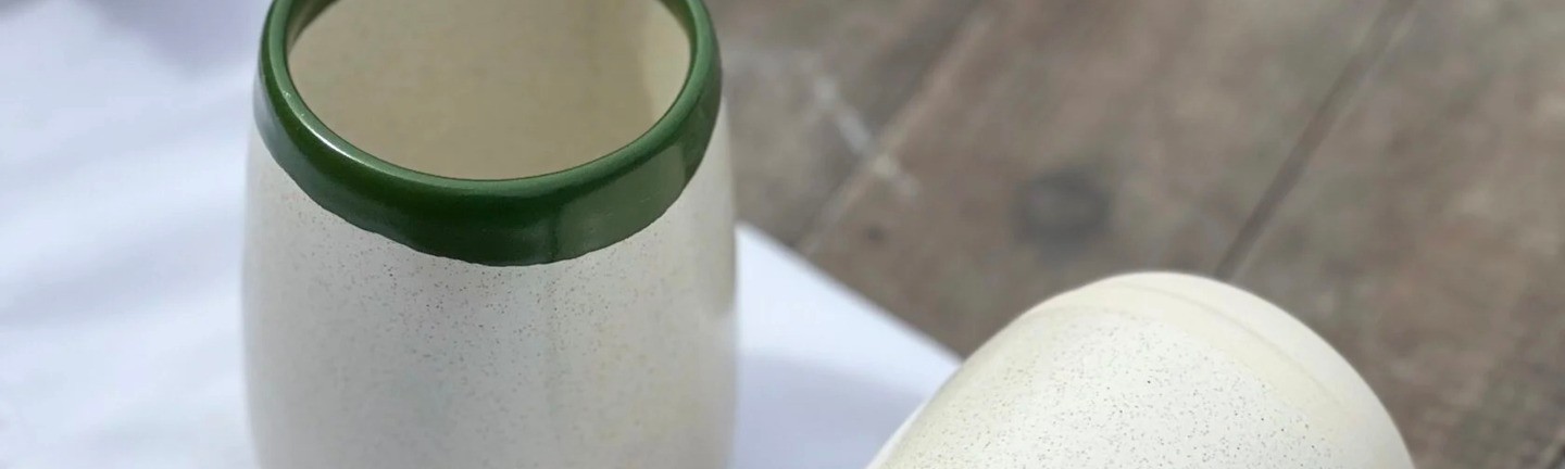 Two ceramic cups with olive rims placed on a white napkin on a wooden table, next to a cotton branch.